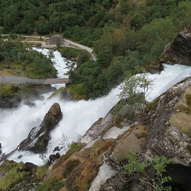 Kraftig foss som bruser nedover en bratt og steinete fjellside med grønn vegetasjon.