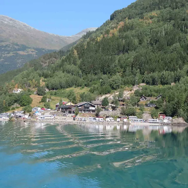 En landsby med hvite hus og båter som ligger tett langs bredden av en blikkstille fjord.