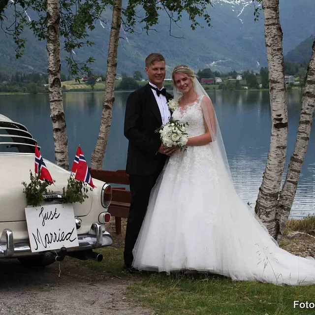 Brudepar poserer ved siden av veteranbil