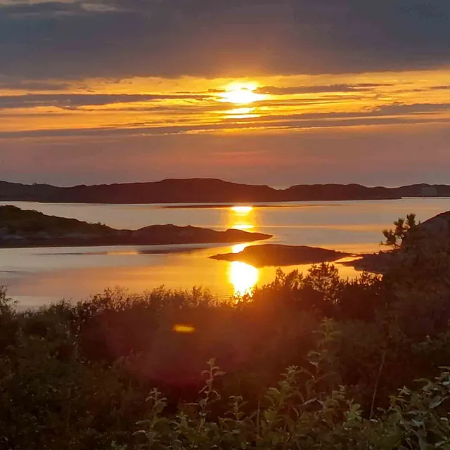Solnedgang over skjærgård og hav, der solen kaster en gyllen lysstripe i det rolige vannet.