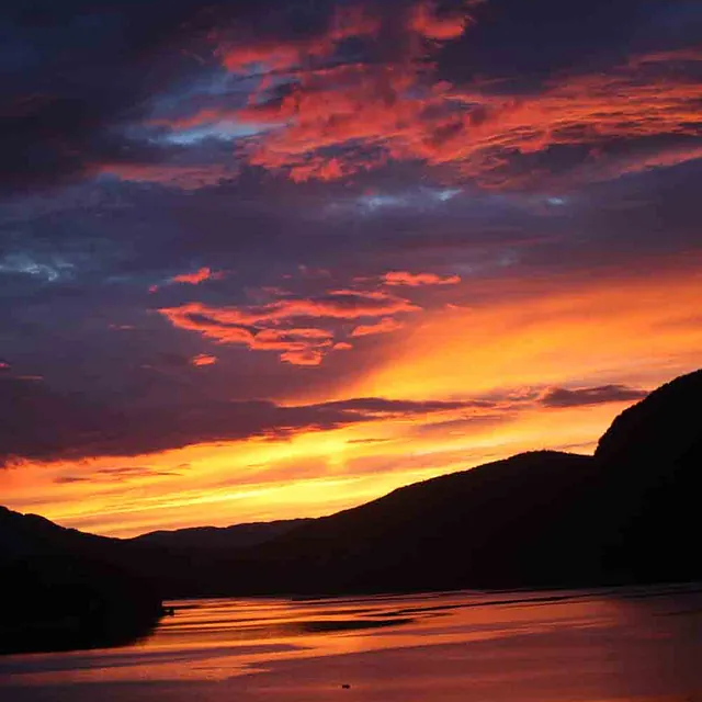 Vertikalt bilde av en fargesprakende solnedgang i lilla og oransje over en mørk fjord.