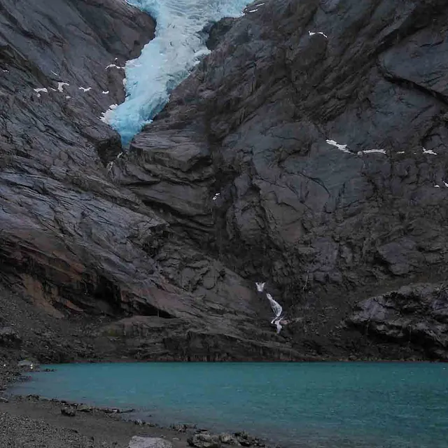 Blå isbre som svinger seg nedover en bratt fjellside mot et grønt brevann.