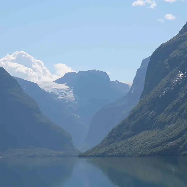 Utsikt fra vannet innover en trang fjord med bratte, dramatiske fjellsider i skygge.