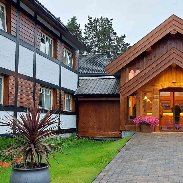 Utvendig fasade av et stort hotell- eller selskapsbygg i tre med en markant inngangsparti og bindingsverksstil.