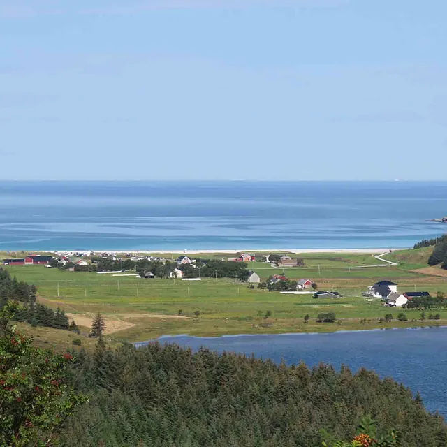 Utsikt over en grønn dal med spredte hus, plassert mellom en innsjø og det åpne havet.