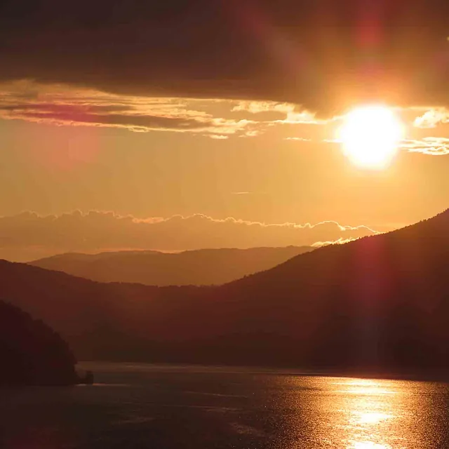 Gyllen solnedgang over mørke fjellrygger som speiler seg i en rolig fjord.
